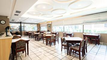 A restaurant with a tiled floor, wooden tables and chairs, and a ceiling with circular light fixtures.