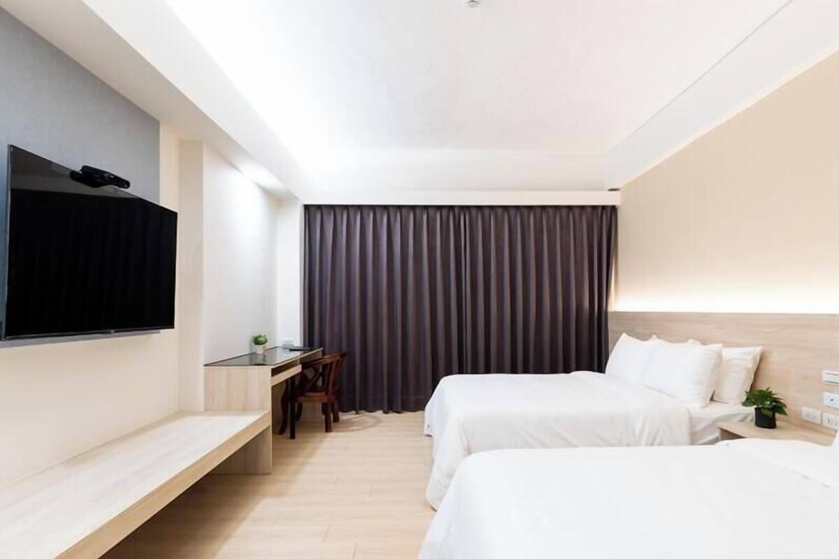A hotel room with a bed, a desk, a chair, a TV, and a large window with curtains.