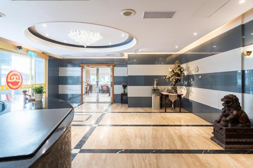 A hotel lobby with a reception desk, a chandelier, a statue, and a wall with a striped pattern.