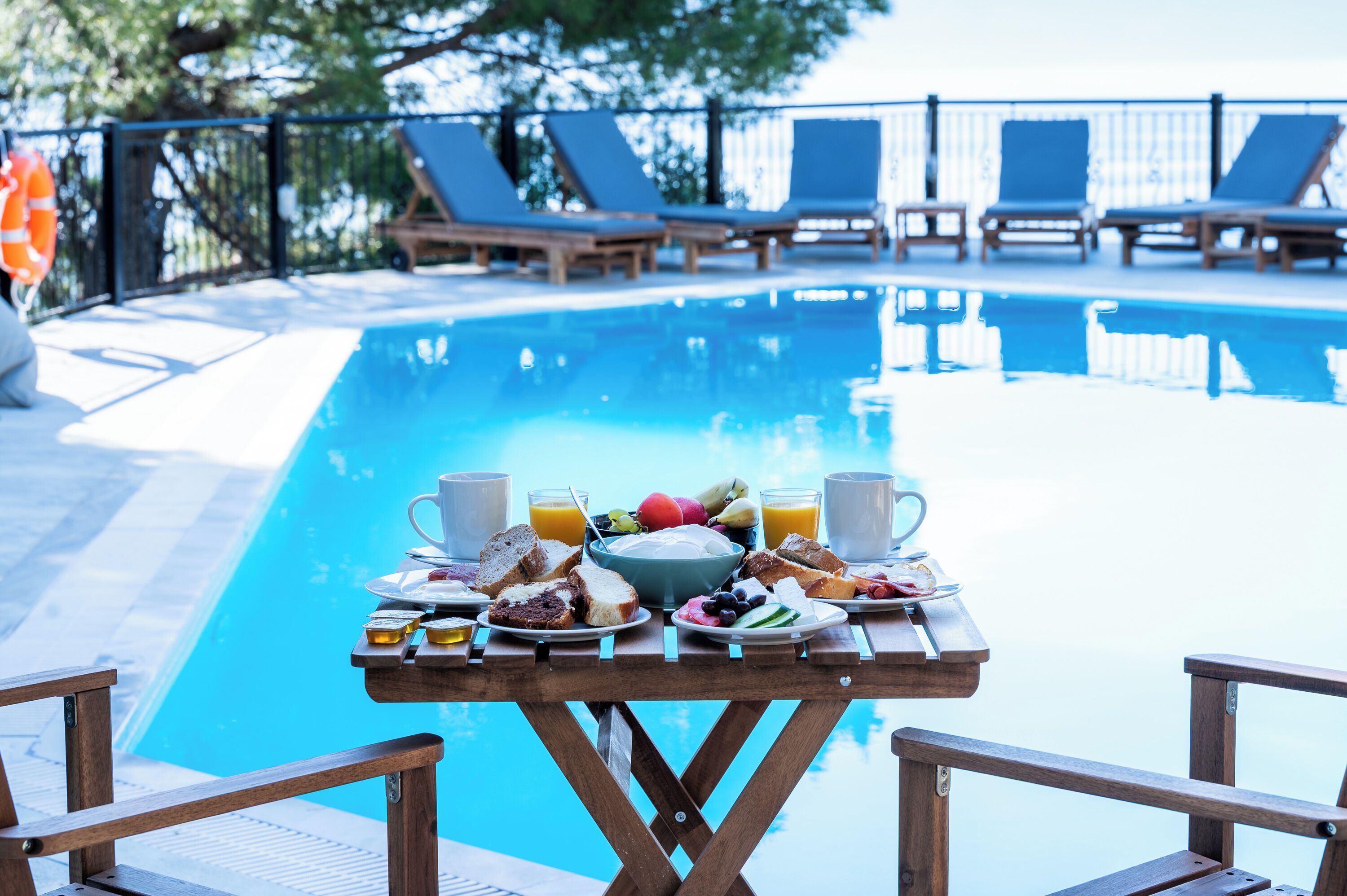 A poolside breakfast table with breakfast items, a pool, and lounge chairs.