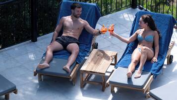 Two lounge chairs by a pool with a wooden table and a metal railing.