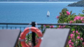 A seaside view with lounge chairs, a life ring, and a sailboat on the water.