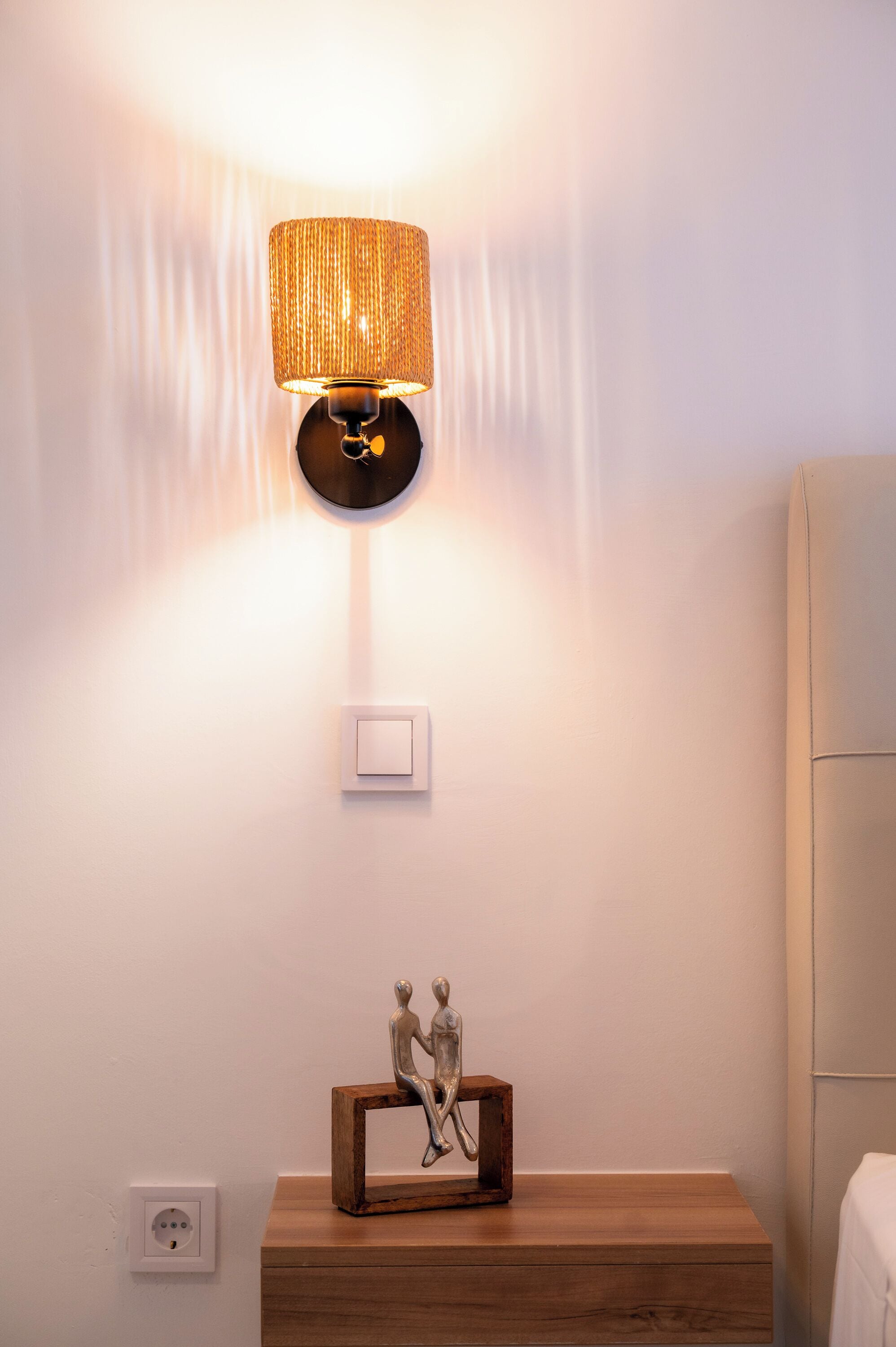 A wall-mounted lamp, a switch, and a wooden nightstand with a figurine.