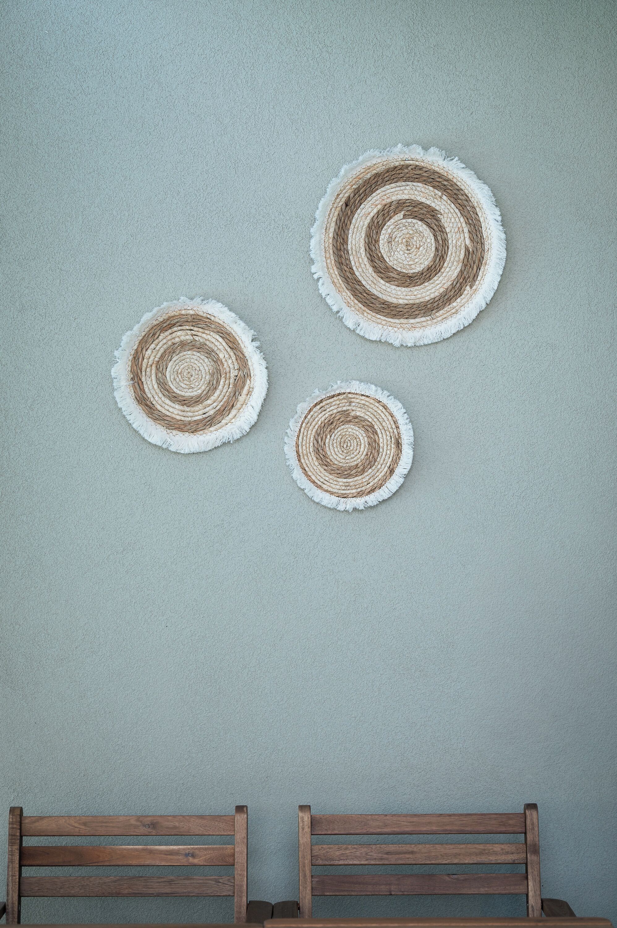 Three circular woven wall hangings on a plain wall.