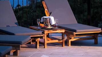 Uma área à beira da piscina com espreguiçadeiras, uma mesa com jarra e copos, e vista para a água e terra ao longe.
