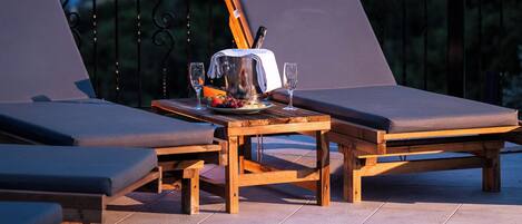 A poolside area with lounge chairs, a table with a pitcher and glasses, and a view of the water and distant land.