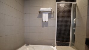 Un baño moderno con una bañera grande, zona de ducha con azulejos negros y un toallero con toallas dobladas.