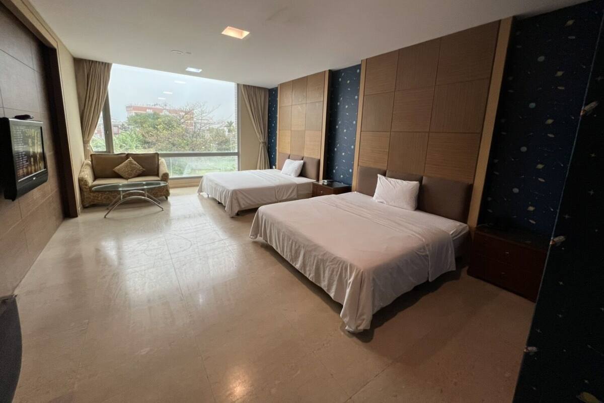 A hotel room with two beds, a sofa, a TV, and a large window with a view.