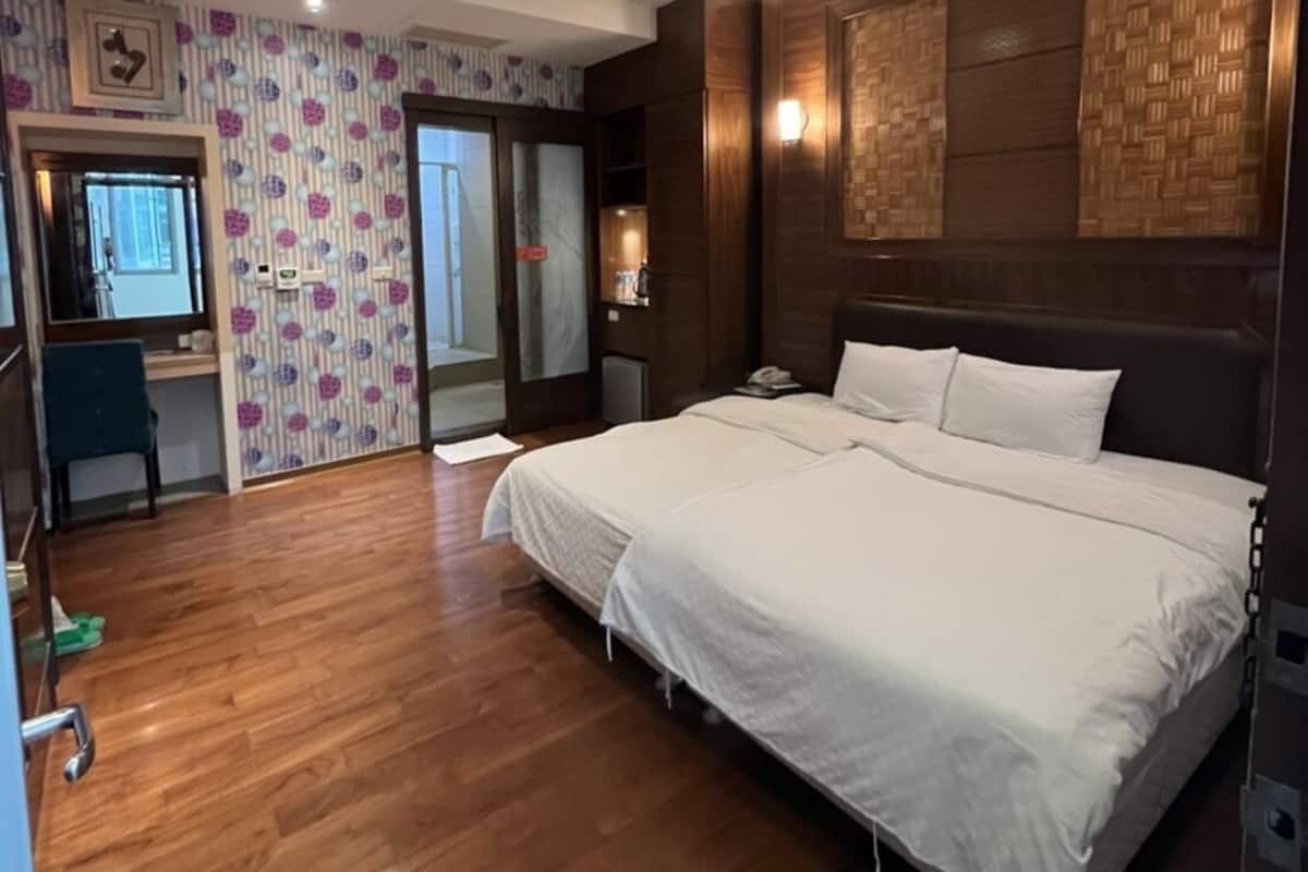 A bedroom with a large bed, wooden flooring, a desk, and a patterned wallpaper.