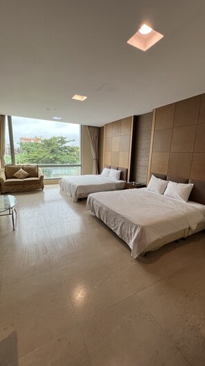 A hotel room with two beds, a sofa, a small table, and large windows offering a city view.