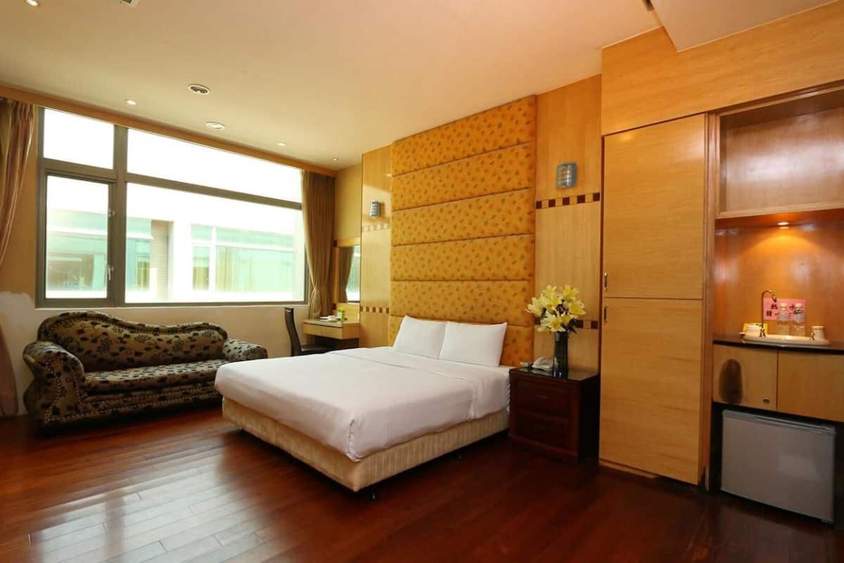 A hotel room with a large bed, a sofa, a desk, and a minibar.