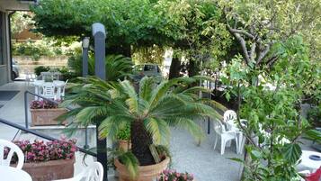 Un espace extérieur aménagé avec des chaises et des tables en plastique blanc, entouré de plantes en pot et d’arbres.