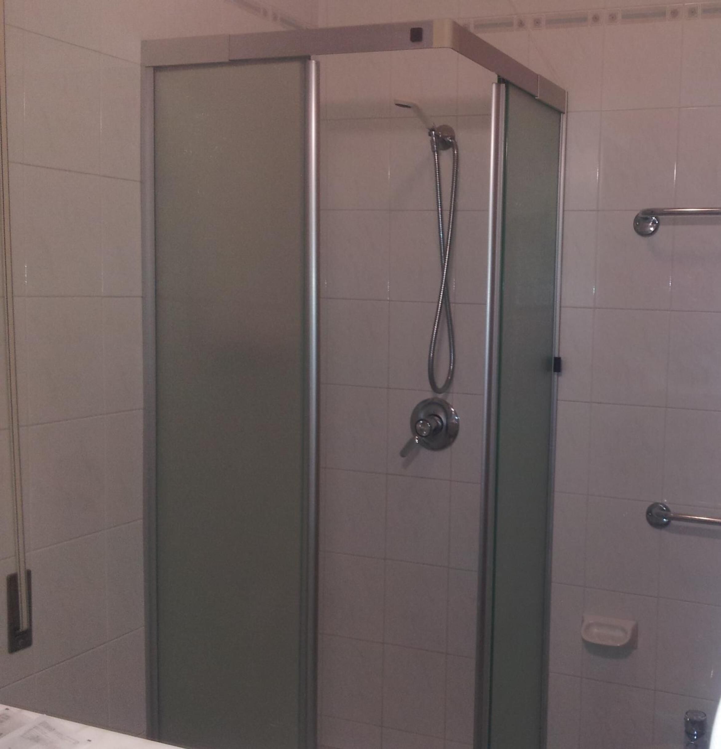 Une cabine de douche fermée par des parois en verre, dotée d’un pommeau de douche à main et d’une barre pour les serviettes.