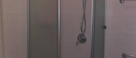 Une cabine de douche fermée par des parois en verre, dotée d’un pommeau de douche à main et d’une barre pour les serviettes.