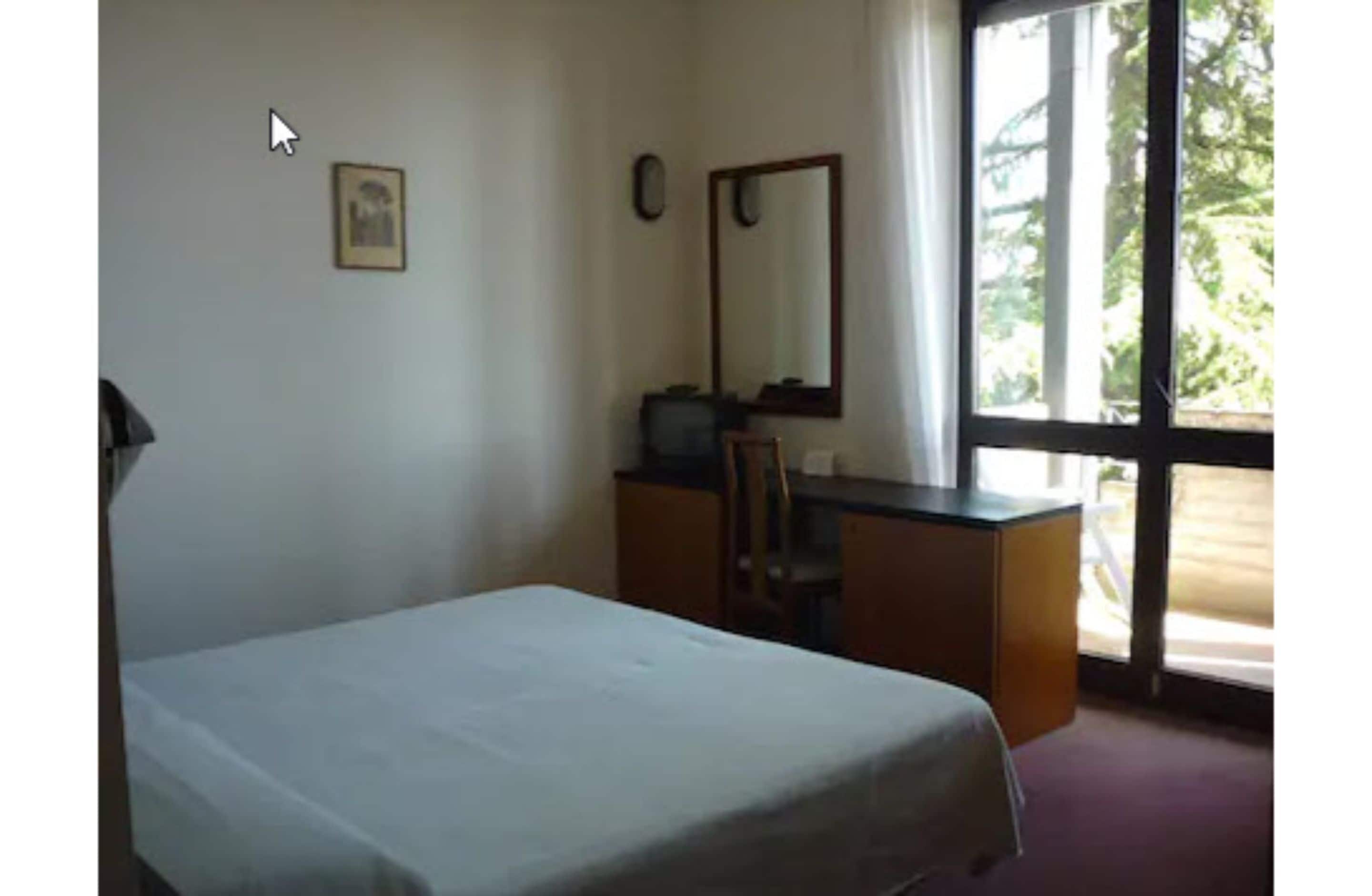 Een kamer met een bed, een bureau, een stoel, een spiegel en een raam.