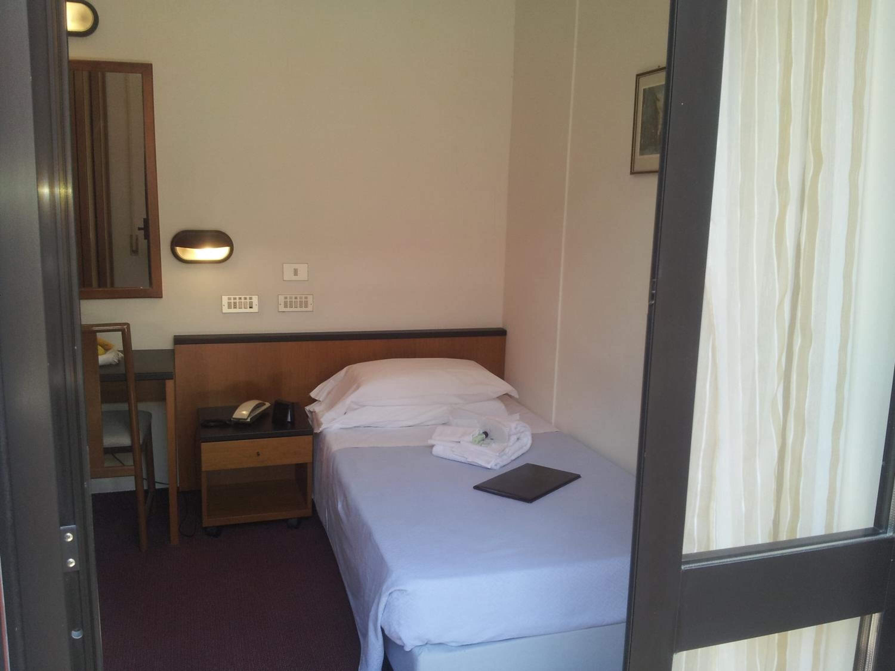 A hotel room with a bed, bedside table, lamp, and a mirror.