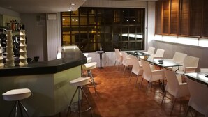 Un espace bar moderne avec un comptoir et des tabourets, un coin salon avec des tables et des chaises, et de grandes fenêtres laissant entrer la lumière naturelle.