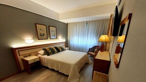 Une chambre d’hôtel comprenant un lit, des tables de chevet, un bureau, une chaise, une télévision et une fenêtre avec des rideaux.