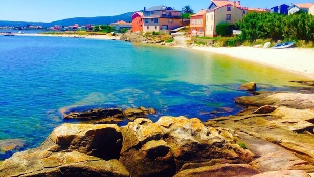 Une zone côtière caractérisée par une eau d’un bleu limpide, un littoral rocheux et des bâtiments aux couleurs vives qui bordent la plage.