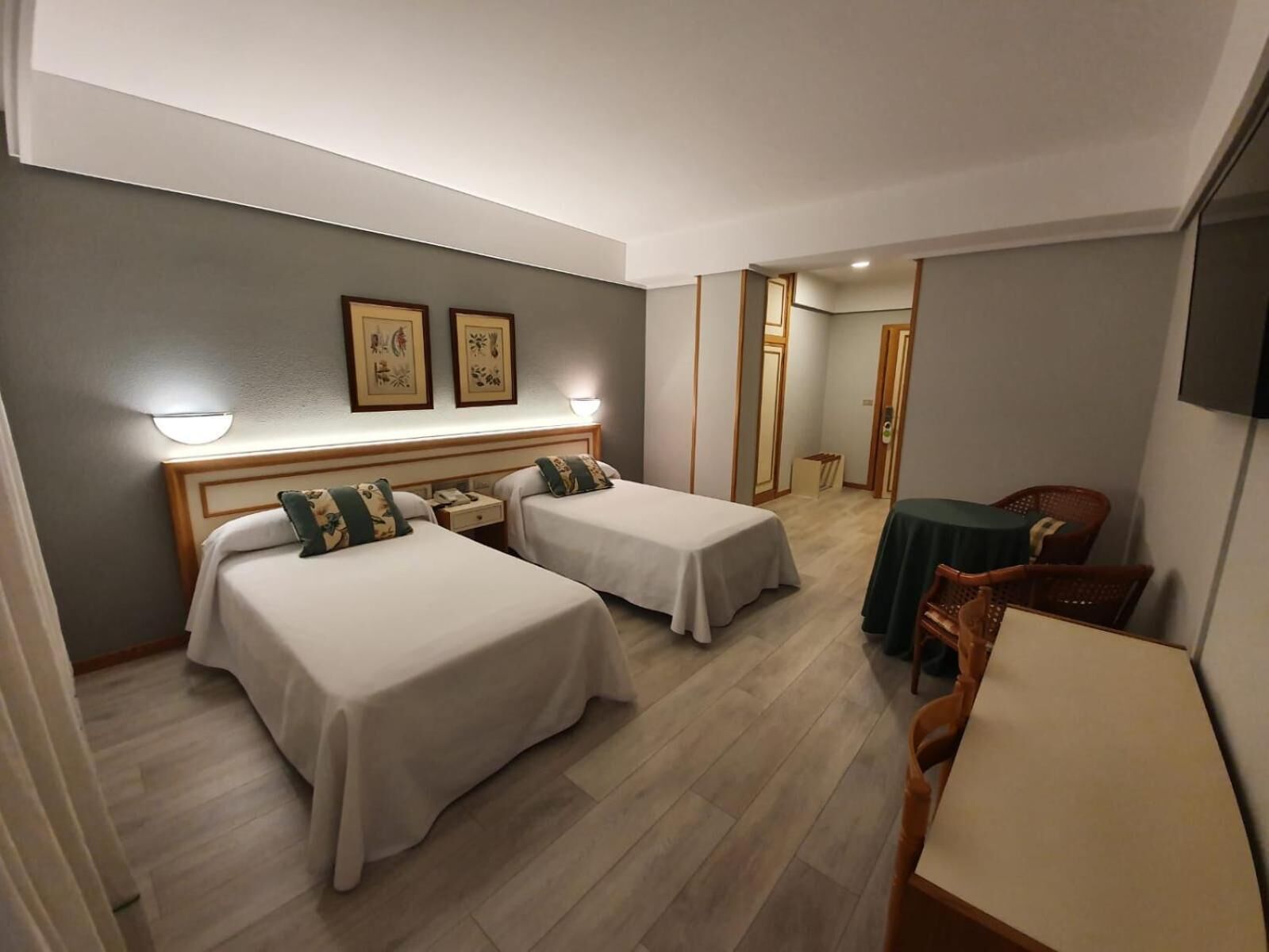 Habitación de hotel con dos camas, un escritorio, una silla y una mesita.