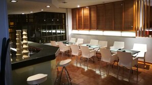 Un espace repas moderne avec un bar, des chaises blanches et un mur en bois doté d’un éclairage intégré.