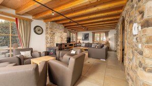 A spacious living area with a stone wall, wooden ceiling beams, and a large window with curtains. - AvenidA Panorama Chalet by Alpin Rentals (Piesendorf)