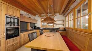 A wooden kitchen with a large table, black chairs, and a hanging light fixture. - AvenidA Panorama Chalet by Alpin Rentals (Piesendorf)