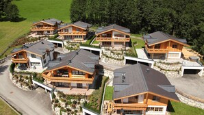 A cluster of modern, wooden houses with balconies, surrounded by a well-maintained garden and a forested area. - AvenidA Panorama Chalet by Alpin Rentals (Piesendorf)