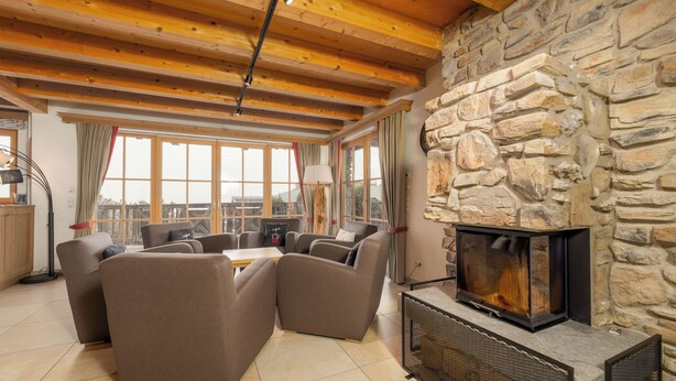 A cozy living room with a stone fireplace, wooden beams, and large windows. - AvenidA Panorama Chalet by Alpin Rentals (Piesendorf)