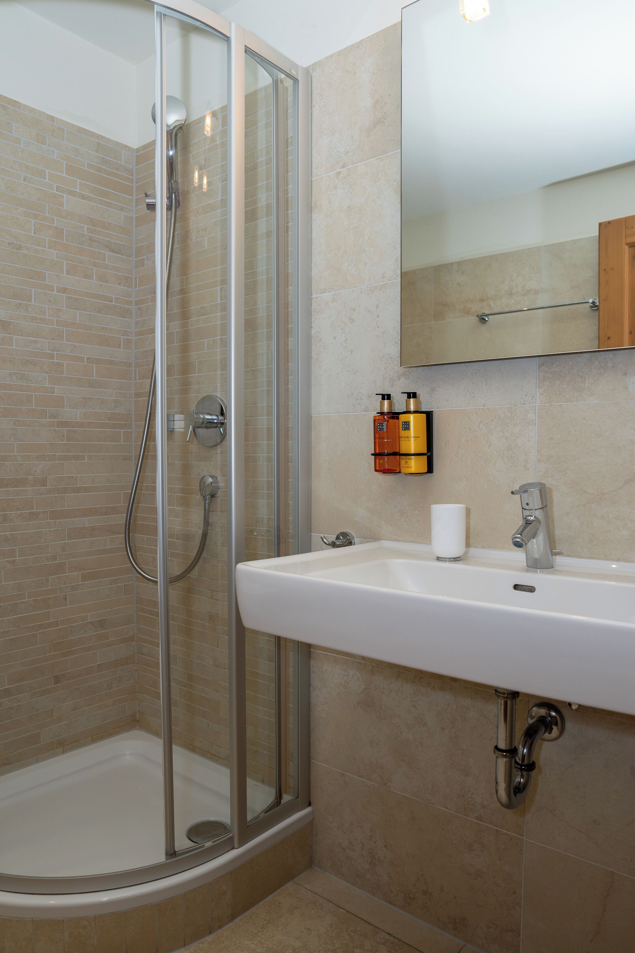 A modern bathroom with a glass-enclosed shower, a white sink, and a mirror above it.