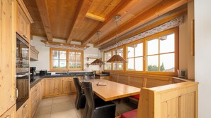 A kitchen with wooden cabinets, a large island with seating, and large windows. - AvenidA Panorama Chalet by Alpin Rentals (Piesendorf)