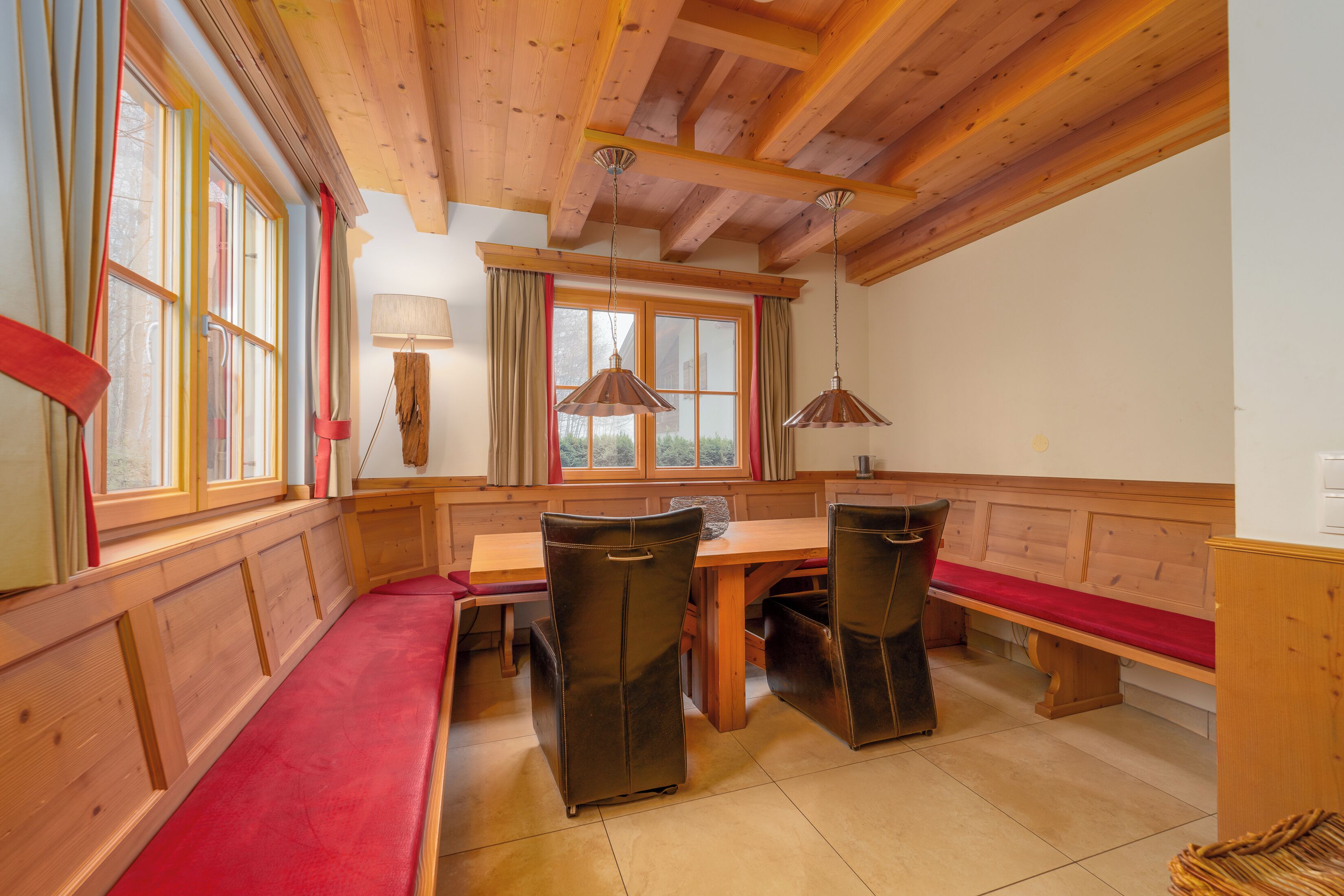 A wooden dining area with benches and a table, wooden ceiling beams, and pendant lights.