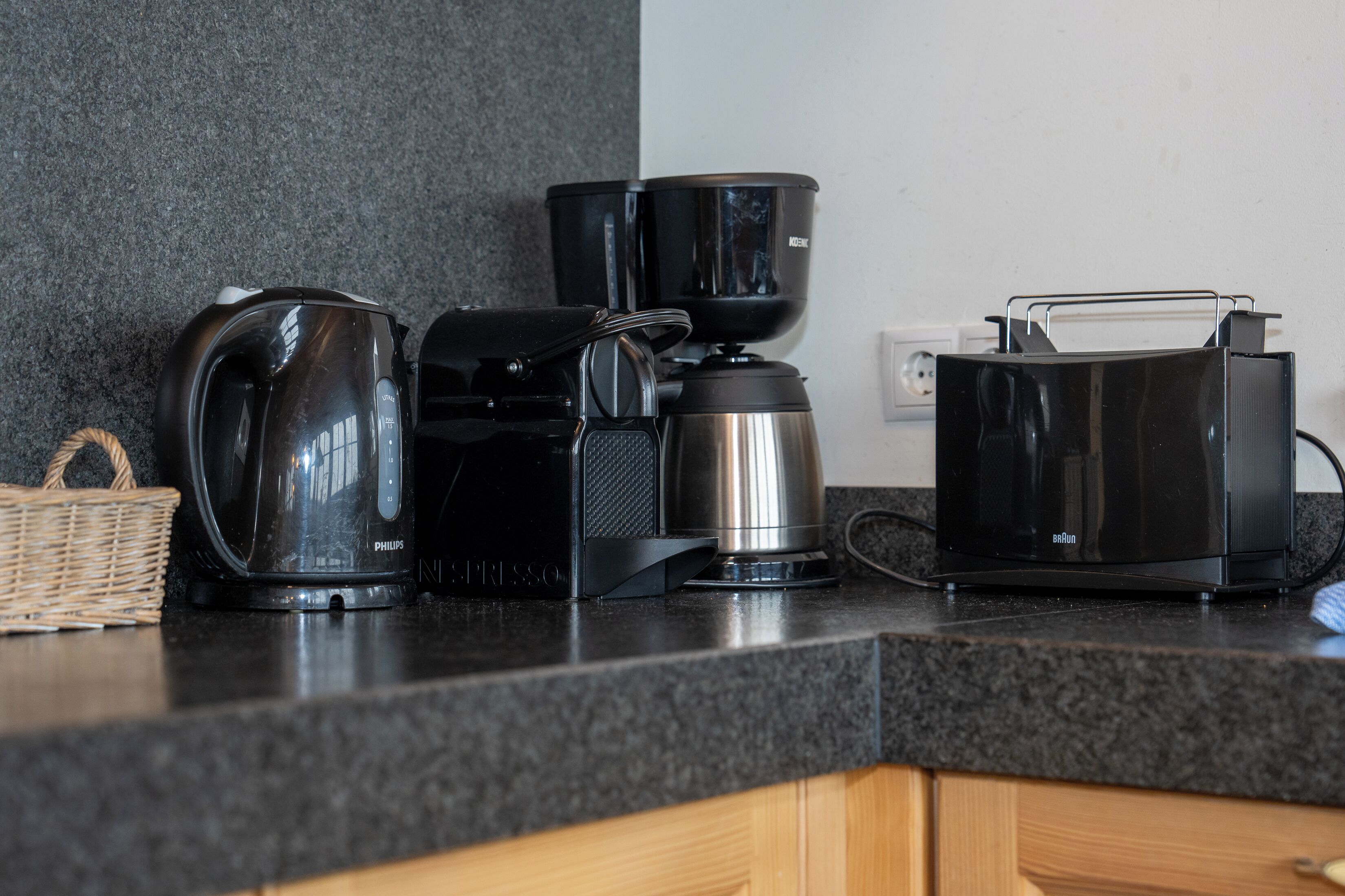 A kitchen counter with a coffee maker, a kettle, a toaster, and a basket.