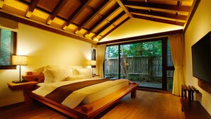 A bedroom with a large bed, wooden beams, a TV, and a view of greenery outside. - Mudanwan Villa (Mudan)