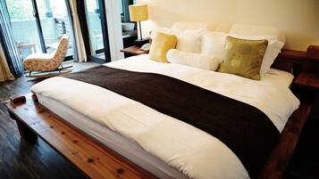 A large bed with a wooden headboard, a bench, a rocking chair, and a lamp.