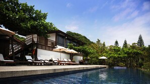 A poolside area with lounge chairs and umbrellas, surrounded by lush greenery and a clear sky. - Mudanwan Villa (Mudan)