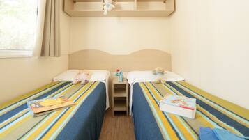Ein Zimmer mit zwei Betten, jeweils mit gestreifter Bettdecke, einem kleinen Regal darüber und einem Fenster mit Vorhängen.