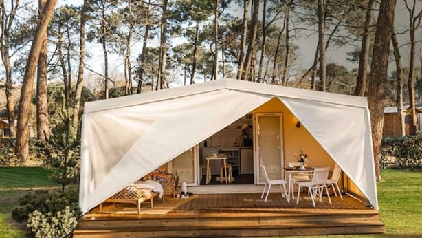 A tent with a wooden deck and white chairs, surrounded by trees. - Camping Serenissima (Mestre)