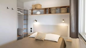 A bedroom with a bed, a wardrobe, a shelf with baskets, and a bedside table. - Camping Serenissima (Mestre)