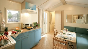 A compact kitchen with blue cabinets, a stove, and a dining area with a table and chairs. - Camping Serenissima (Mestre)