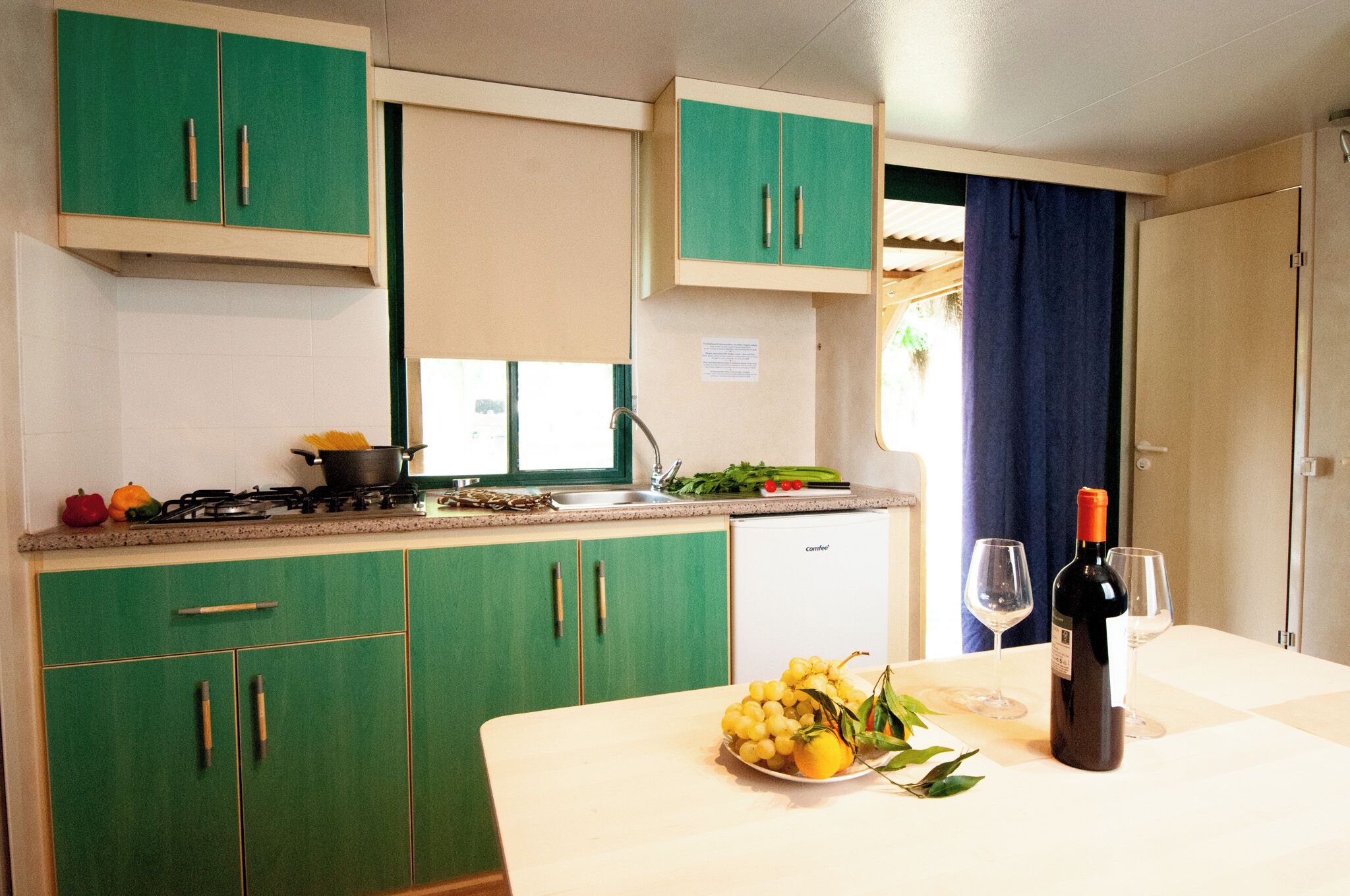 A compact kitchen with green cabinets, a gas stove, a sink, and a dining area with a table set for two.