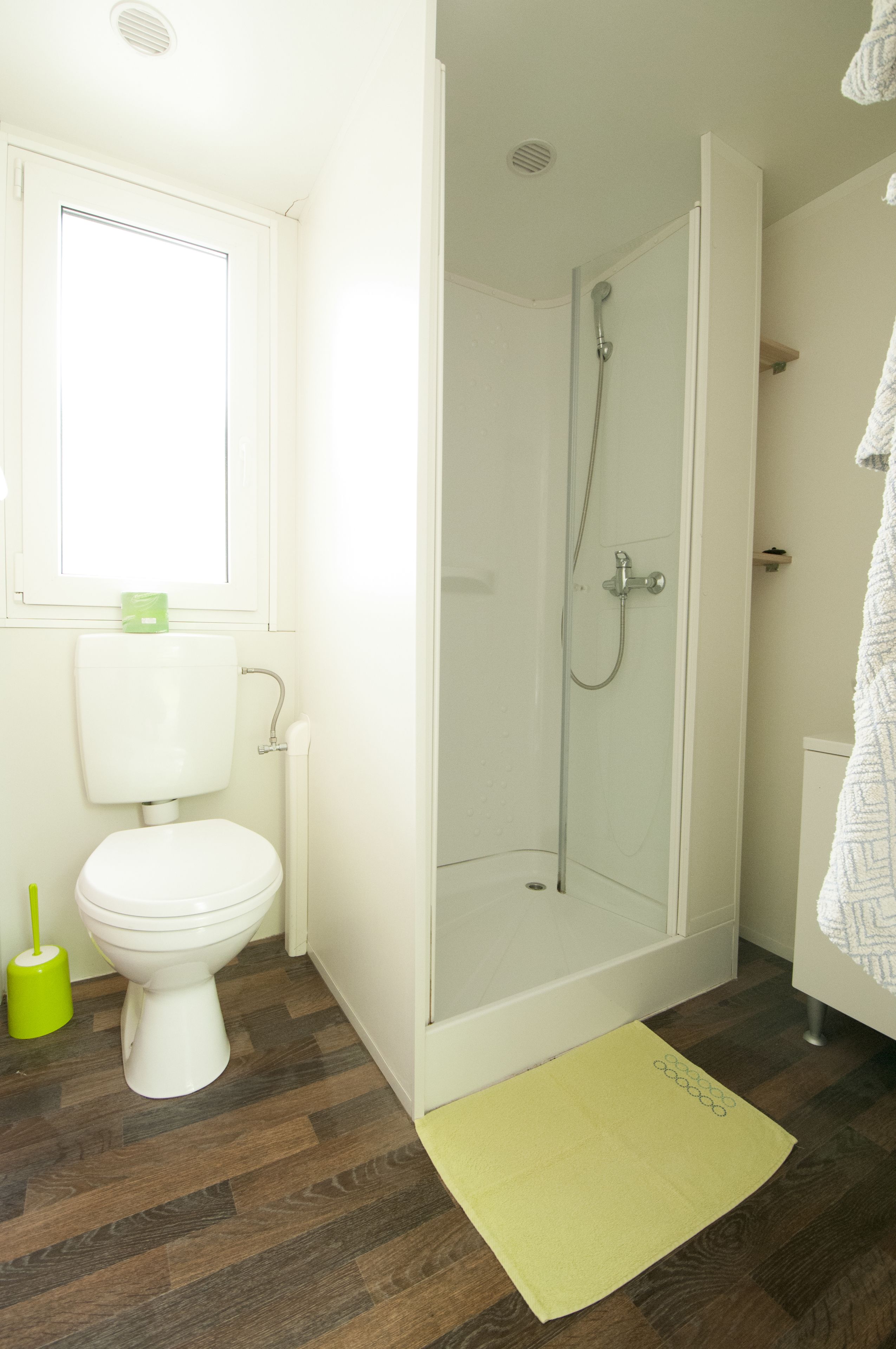 A bathroom with a toilet, shower, and a yellow mat on the floor.