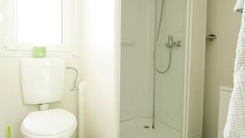 A bathroom with a toilet, shower, and a yellow mat on the floor.
