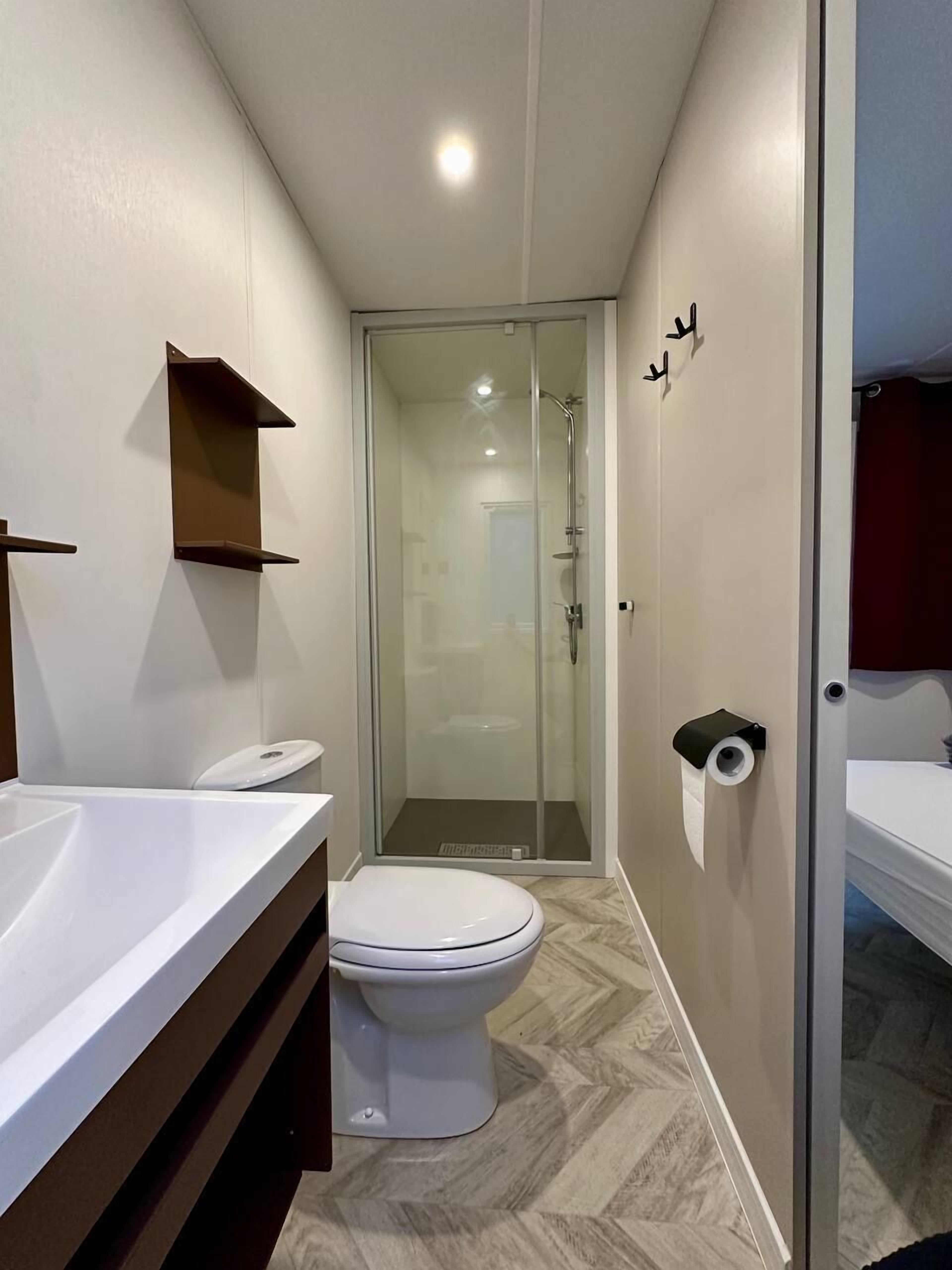 A narrow bathroom with a toilet, a shower, and a sink.