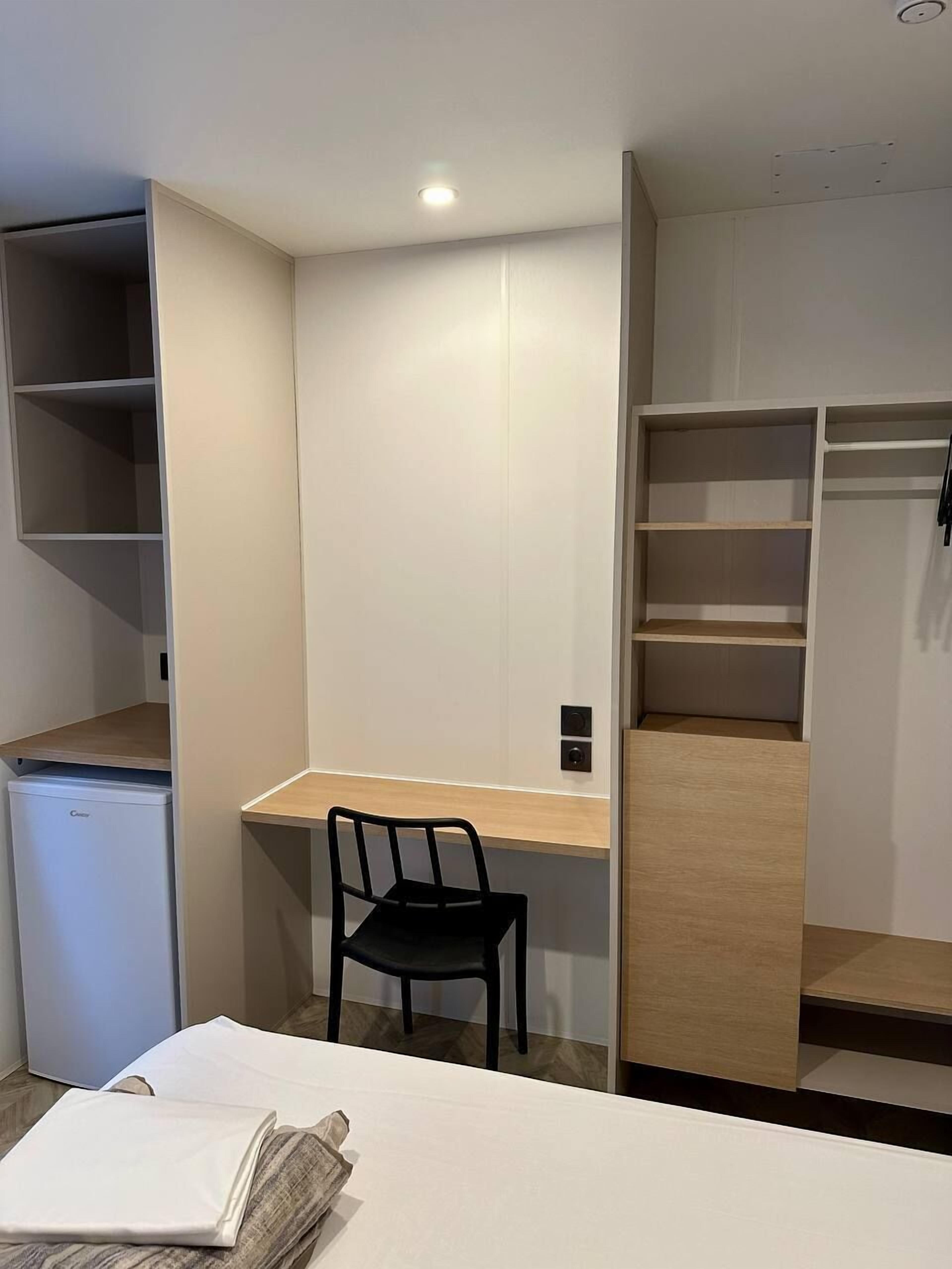 A compact room with a small desk, a chair, and a compact refrigerator.