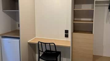 A compact room with a small desk, a chair, and a compact refrigerator.