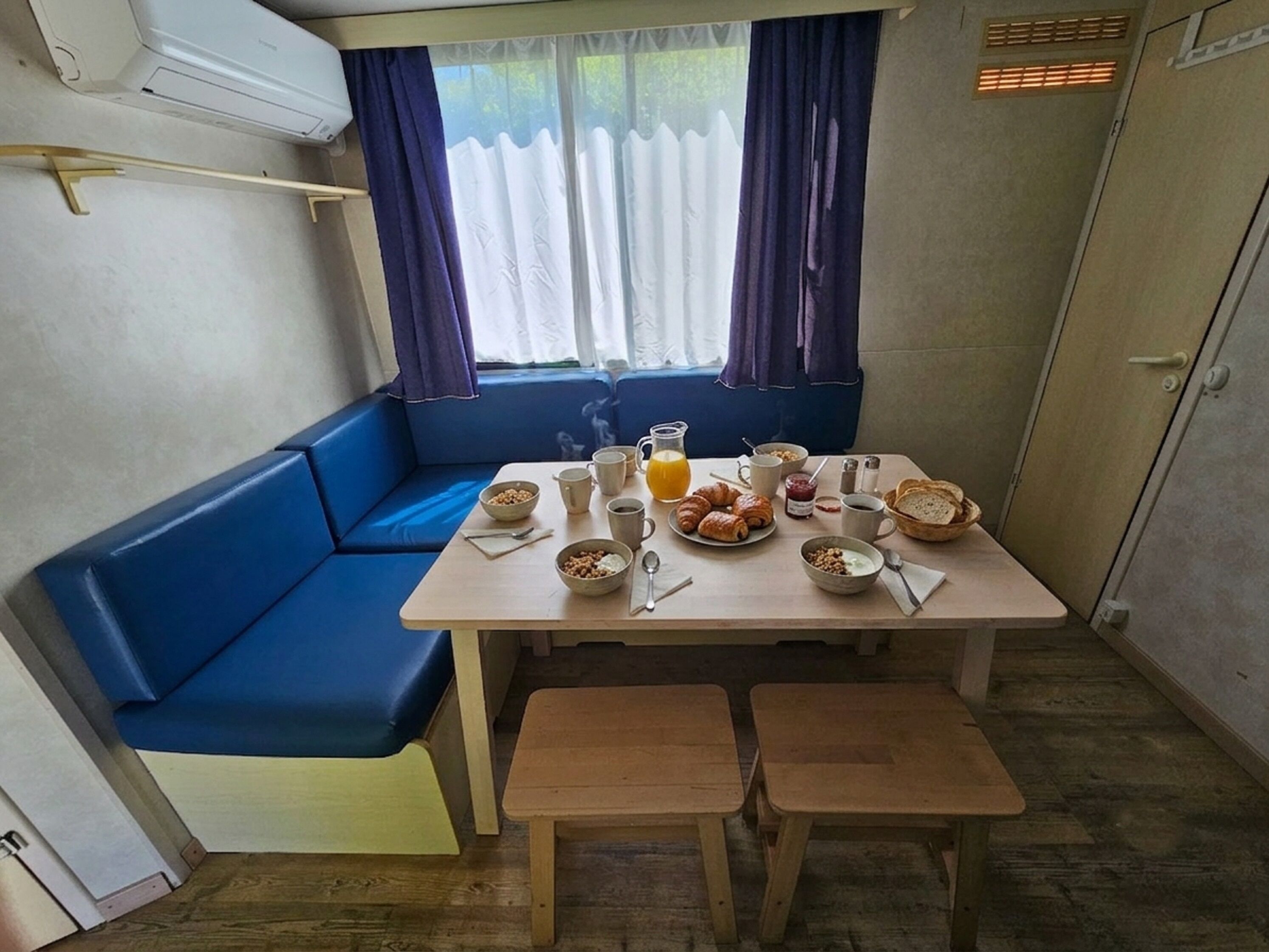 A small kitchenette with a table set for breakfast, a blue sofa, and a window with curtains.
