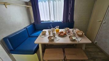 A small kitchenette with a table set for breakfast, a blue sofa, and a window with curtains.