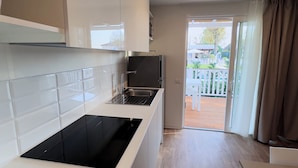 A modern kitchen with white cabinets, a black induction cooktop, and a stainless steel sink. - Camping Serenissima (Mestre)