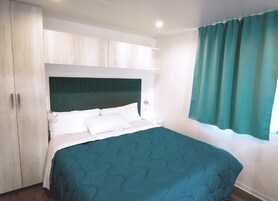 Un dormitorio con cama, cabecera, armario y ventana con cortinas.